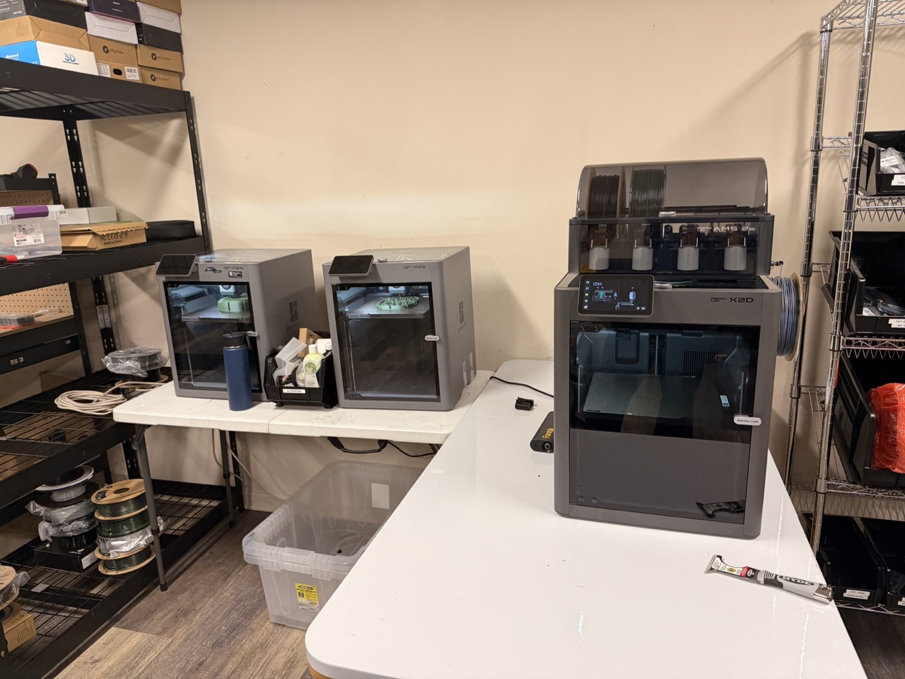 Three enclosed 3D printers, including a multi-material unit, on the prototyping bench in the Waypoint Telemetry lab with filament spools and parts shelving