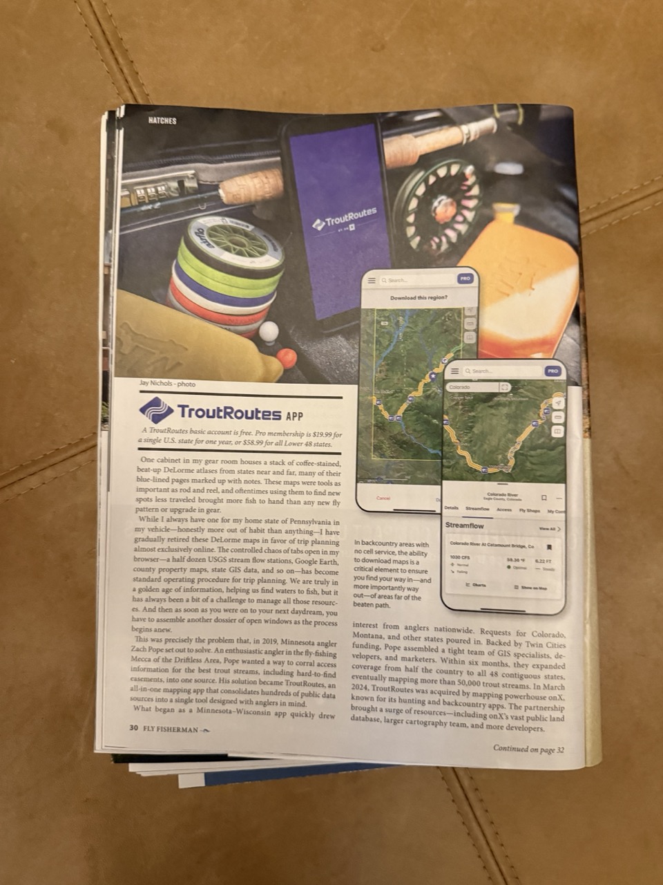 Fly Fisherman magazine feature on the TroutRoutes app founded by Zachary Pope, showing the app on a phone beside a fly reel and tippet spools